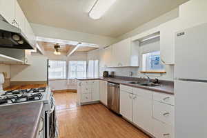 ACTUAL KITCHEN featuring under cabinet range hood, white appliances, a sink, white cabinets, and dark countertops