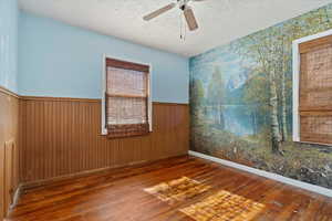 Unfurnished room with wood-type flooring, a wainscoted wall, ceiling fan, and a textured ceiling