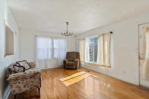 Sitting room with a textured ceiling, baseboards, hardwood / wood-style flooring, and an inviting chandelier