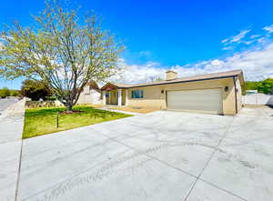 Single story home featuring an attached garage, brick siding, a front yard, a chimney, and concrete driveway