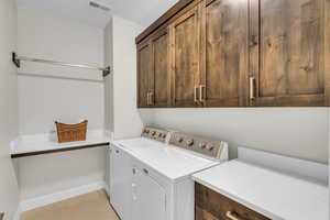 Laundry room featuring cabinet space, light tile patterned floors, baseboards, visible vents, and independent washer and dryer