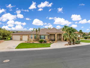 View of front of property featuring a garage, stone siding, driveway, stucco siding, and a front yard