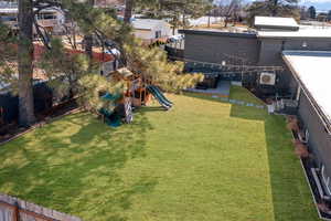 View of the fully fenced backyard with a hot tub, string lights, and a playground.