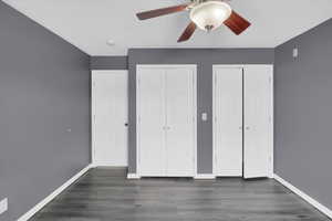 Unfurnished bedroom with a ceiling fan, baseboards, two closets, and wood finished floors