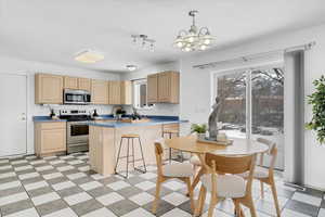 Kitchen featuring appliances with stainless steel finishes, light brown cabinets, visible vents, and a notable chandelier