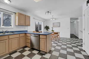 Kitchen featuring light brown cabinets, stainless steel dishwasher, dark countertops, and a sink