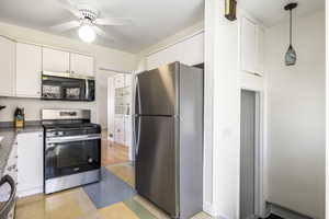 Kitchen with dark countertops, hanging light fixtures, appliances with stainless steel finishes, a ceiling fan, and white cabinets