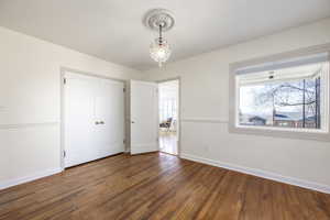 Unfurnished bedroom featuring a notable chandelier, a closet, hardwood / wood-style flooring, and baseboards