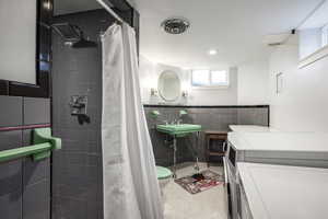 Full bathroom featuring speckled floor, visible vents, tile walls, a tile shower, and washer / clothes dryer