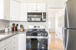 Kitchen featuring appliances with stainless steel finishes, tasteful backsplash, white cabinets, and wood finished floors