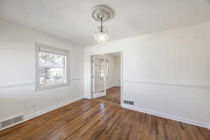 Spare room with wood-type flooring, visible vents, a notable chandelier, and baseboards