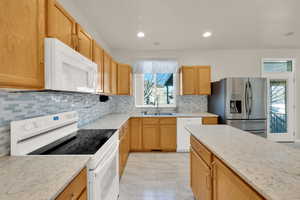 Kitchen with light stone countertops, white appliances, tasteful backsplash, and a sink