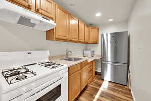 Kitchen featuring white appliances, light countertops, light wood-type flooring, under cabinet range hood, and a sink