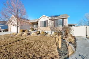 Single story home featuring stucco siding, concrete driveway, an attached garage, a gate, and roof mounted solar panels