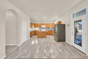 Kitchen with a center island, light countertops, backsplash, white microwave, and freestanding refrigerator