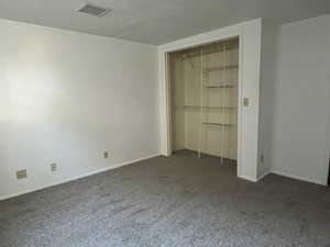 Unfurnished bedroom featuring dark colored carpet, a closet, and visible vents