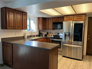 Kitchen featuring light wood finished floors, dark countertops, a peninsula, stainless steel appliances, and a sink