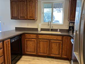 Kitchen with a sink, black dishwasher, light wood-type flooring, freestanding refrigerator, and dark countertops