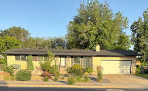 Ranch-style house featuring brick siding, a garage, concrete driveway, and a chimney