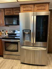 Kitchen featuring dark countertops, light wood finished floors, appliances with stainless steel finishes, and brown cabinetry