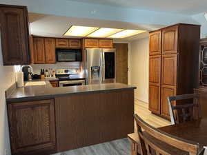 Kitchen featuring stainless steel appliances, a peninsula, a sink, light wood-style floors, and dark countertops