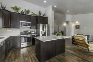 Kitchen with dark wood-style floors, light countertops, appliances with stainless steel finishes, a kitchen island, and dark brown cabinets