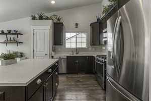 Kitchen featuring appliances with stainless steel finishes, dark wood-type flooring, light stone countertops, open shelves, and a sink