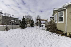 Yard covered in snow with fence and a pergola