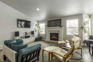 Living room with light wood-type flooring, a glass covered fireplace, visible vents, and baseboards