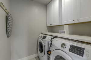 Clothes washing area featuring cabinet space, light tile patterned flooring, baseboards, and washing machine and clothes dryer