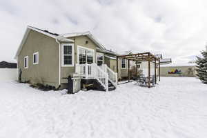 Snow covered property featuring fence, a pergola, and stucco siding