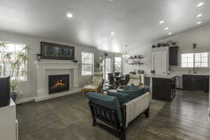 Living area with baseboards, a glass covered fireplace, lofted ceiling, dark wood-style flooring, and recessed lighting