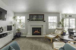 Living room featuring baseboards, a glass covered fireplace, and light colored carpet