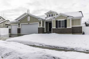 View of front facade with an attached garage, fence, board and batten siding, and brick siding