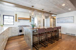 Kitchen with light wood-style flooring, an island with sink, high end range, and light stone countertops