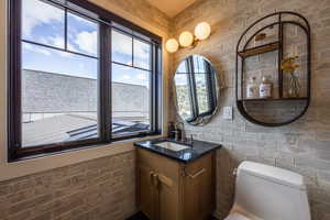 Bathroom featuring toilet, vanity, and brick wall