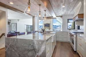 Kitchen with dark wood-style floors, wooden ceiling, light stone countertops, a large island with sink, and high end white range