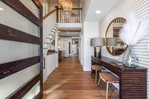 Hall featuring a towering ceiling, stairs, wood finished floors, and recessed lighting