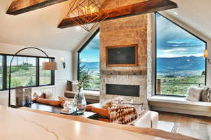 Living room with lofted ceiling with beams, a chandelier, a stone fireplace, a wainscoted wall, and wood finished floors