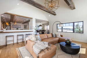 Living room featuring a notable chandelier, beamed ceiling, wood finished floors, and a decorative wall