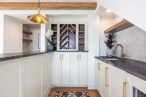 Kitchen with light wood-style flooring, a sink, decorative backsplash, open shelves, and dark stone countertops