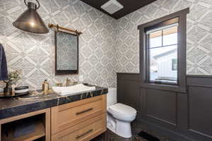 Bathroom featuring toilet, wallpapered walls, and vanity