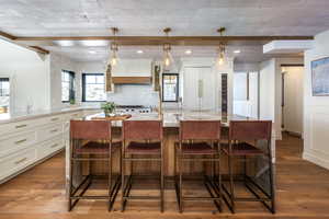 Kitchen featuring a breakfast bar, wood finished floors, white cabinets, tasteful backsplash, and beamed ceiling