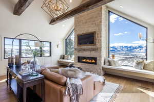 Living area featuring beam ceiling, visible vents, an inviting chandelier, a stone fireplace, and wood finished floors