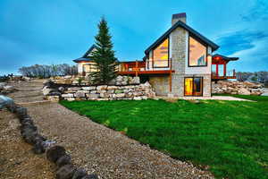 Rear view of property with stone siding, a yard, a chimney, and a wooden deck