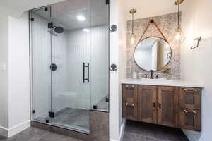 Full bath with tasteful backsplash, a stall shower, vanity, tile patterned flooring, and baseboards