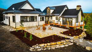 Back of property featuring a patio, a chimney, a standing seam roof, metal roof, and stone siding