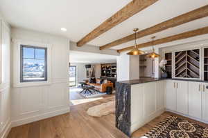 Kitchen featuring dark stone countertops, decorative light fixtures, light wood-type flooring, a decorative wall, and beam ceiling