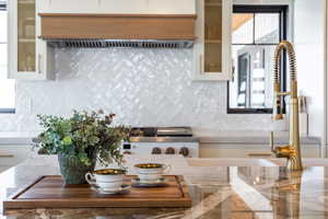 Kitchen with ventilation hood, glass insert cabinets, white cabinets, and tasteful backsplash