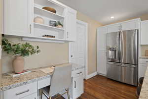 Kitchen featuring dark wood-style floors, stainless steel fridge, white cabinets, and built in study area